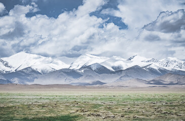 Landscape in the Pamir Mountains of Tajikistan with snow, glaciers, and cliffs, a panorama of mountains in cloudy weather for the background, nature in the Tien Shan highlands, landscape background