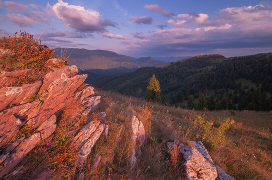 View of the sun kissing rugged rocks and golden grasses atop rolling hills under a pastel sky, Nova Hola, Banska Bystrica Region, Slovakia.