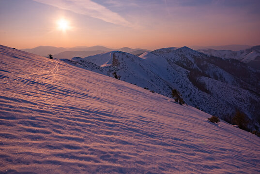 View of snow-covered mountains bathed in the warm glow of the sunset, with visible trails, Rovna hola, Banskobystricky kraj, Slovakia.