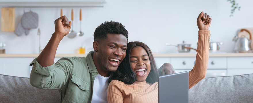 A joyful couple sits on a couch, raising their hands in celebration while watching a screen. Their expressions show happiness and excitement in a cozy living room setting. - Powered by Adobe