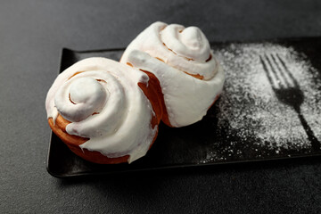 Fragrant cinnabons with cream on a black rectangular plate on a gray background