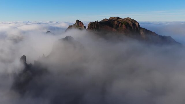 Drone glides above Madeira, Portugal, over Pico do Arieiro pinnacles as fog drifts, peaks appear and vanish, a faint fogbow forms, soft morning light and wide panorama