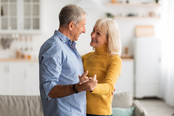 Fototapeta premium A happy couple dances closely together in their warm living room. Sunlight fills the space as they share smiles and laughter, creating a joyful atmosphere in their home.