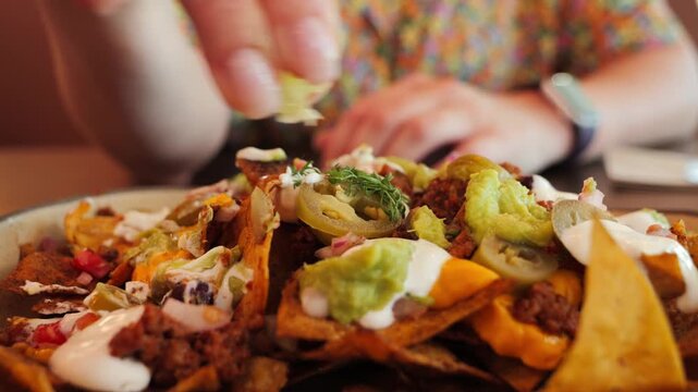 Delicious nachos with beef, melted cheese, jalapenos, onions and herbs. A woman takes a lime wedge and splashes the juice on nachos. The perfect snack. High quality 4k footage