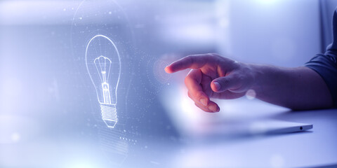 A hand reaches toward a glowing digital lightbulb hologram icon. Concept of innovation, creativity,...