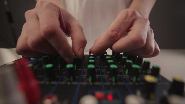 Close-up hands of sound engineer adjusting multiple knobs and levels on professional audio mixing console, fine-tuning volume and equalization for live performance or studio recording.