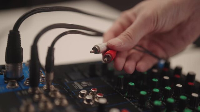 Close-up of sound engineer connecting RCA audio cables to mixing console, setting up professional music production equipment for recording, broadcasting, live event sound distribution, slow motion.