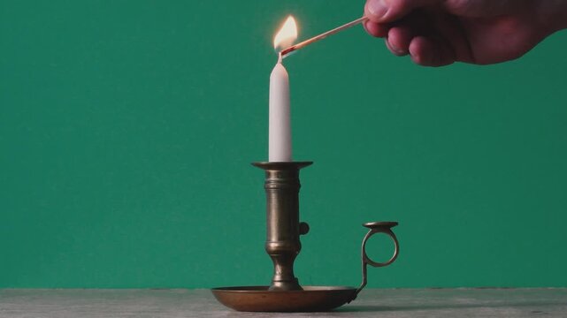 light a candle with a match in an antique brass candlestick