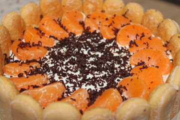 Colorful cake with orange slices and chocolate shavings arranged on top of ladyfinger biscuits during a festive gathering