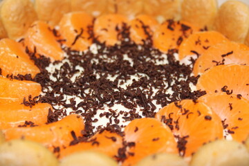 Dessert features chocolate shavings and orange slices arranged on cream topping, served in a round dish at a gathering