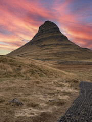 Kirkjufell mountain under a vibrant sunset sky painted in orange, red, and pink hues, creating a dramatic and colorful Icelandic landscape.