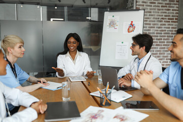 Fototapeta premium Attractive african american woman doctor leading international team of physicians, multiracial team of medical staff having professional training at clinic, discussing various medical cases