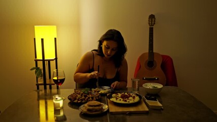 A young woman enjoys a delicious dinner at home, complete with red wine. The warm, cozy lighting and an acoustic guitar in the background create a perfectly relaxed and intimate evening setting.