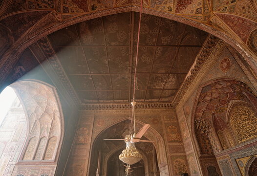 View of intricate Mughal architecture bathed in soft light, with ornate arches framing glimpses of the outside world, Lahore, Punjab, Pakistan.