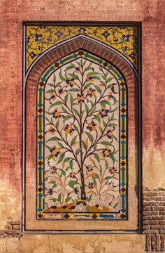 View of an ornate mosaic tree with vibrant floral accents set within a stone archway, framed by weathered brickwork, Lahore, Punjab, Pakistan.