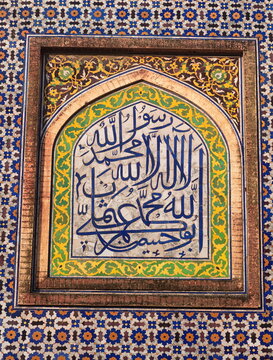 View of intricate Islamic calligraphy framed with vibrant yellow and green floral patterns against a backdrop of geometric tilework, Lahore, Punjab, Pakistan.