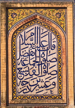 View of intricate Arabic calligraphy in blue against a weathered yellow and white tiled archway, framed by aged bricks, Lahore, Punjab, Pakistan.