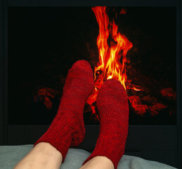 Winter scene with legs in red woolen socks resting near glowing fireplace. Feelings of relaxation.