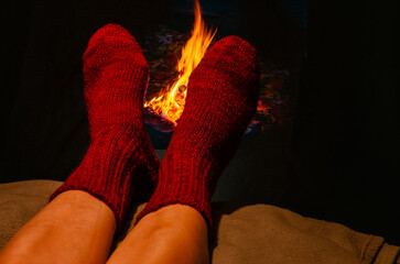 Winter scene with legs in red woolen socks resting near glowing fireplace. Feelings of relaxation.