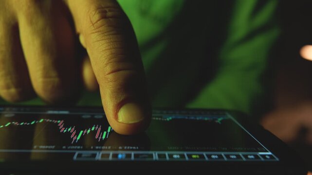Close-up of a trader's finger scrolling through a financial graph on a digital device at night