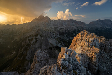 Aerial view of jagged peaks catching the golden light against a backdrop of dramatic clouds over the Julian Alps, Triglav, Gorenjska, Slovenia.