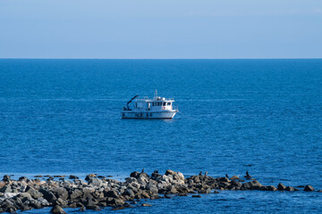 A solitary boat floats peacefully on calm blue waters near a rocky jetty under a clear sky.