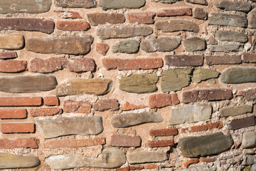 A close-up of a rustic wall reveals a mix of weathered stones and reddish bricks arranged in a textured pattern.