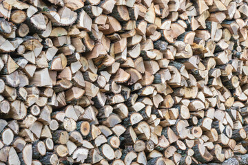 A dense stack of split firewood reveals varied textures and earthy tones in a rustic outdoor setting.