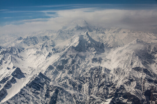 Aerial view of majestic, snow-capped mountains piercing through a blanket of clouds, their peaks kissed by the soft, ethereal light of the sun, Skardu, Gilgit Baltistan, Pakistan.