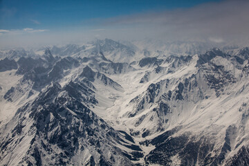 Aerial view of the rugged, snow-dusted mountains under a pale sky, creating a stark contrast of textures and tones in the landscape, Skardu, Gilgit Baltistan, Pakistan.