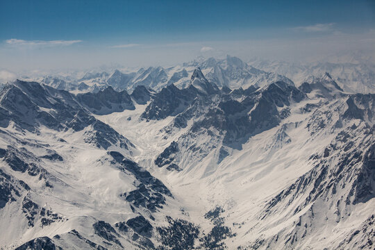 Aerial view of snow-capped peaks and valleys create a stark, majestic landscape under a clear sky, contrasting the rugged terrain with the soft snow, Skardu, Gilgit Baltistan, Pakistan.