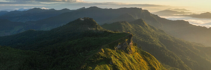 Aerial view of sunlit peaks pierce through the morning mist, casting long shadows across the verdant landscape, Tambon Tap Tao, Chang Wat Chiang Rai, Thailand.