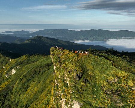 Aerial view of people atop the cliff of Phu Chi Fa, bathed in the soft glow of dawn, overlooking the mountain range, Tambon Tap Tao, Chang Wat Chiang Rai, Thailand.
