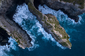 Aerial view of rugged cliffs meeting the turbulent ocean, where the dark rocks contrast with the frothy white waves, Ribeirinha, Azores, Portugal.