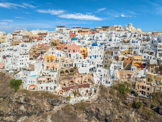 Aerial view of whitewashed buildings cascading down the cliffside, dotted with blue-domed churches under a clear sky, Oia, Thira, Greece.