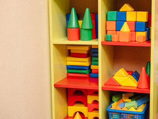 Bright colorful plastic blocks and toys organized on a yellow shelf in a child's playroom or nursery