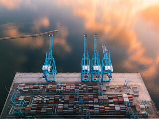 Aerial view of towering blue cranes oversee a grid of colorful shipping containers under a sky mirroring the water's surface, Rijeka, Primorje-Gorski Kotar County, Croatia.