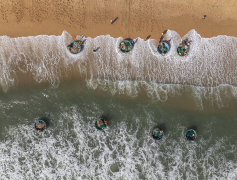 Aerial view of coracle boats resting on the sandy shore as the turquoise waves roll in, creating a mesmerizing contrast of colors and textures, Quy Nhon, Binh Dinh, Vietnam.