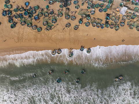 Aerial view of colorful coracle boats dotting the sandy shore and turquoise waters, a vibrant tapestry where the land meets the sea, Quy Nhon, Binh Dinh, Vietnam.