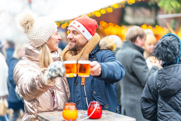 Smiling couple holding festive punch and mulled wine mugs enjoying winter warmth with a Christmas...