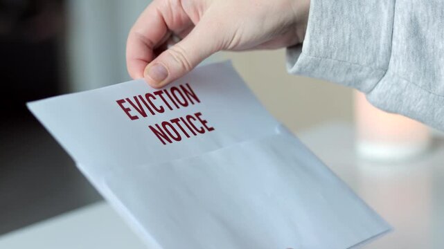 Close-up of a person pulling an eviction notice letter from a white envelope. Concept of housing issues, rental problems, eviction process, financial hardship, legal documents, and real estate crisis