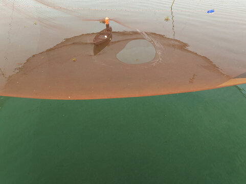 Aerial view of the water surface with a net, showing a contrast between the brown colored top water and the green bottom water, Hội An, Quảng Nam, Vietnam.