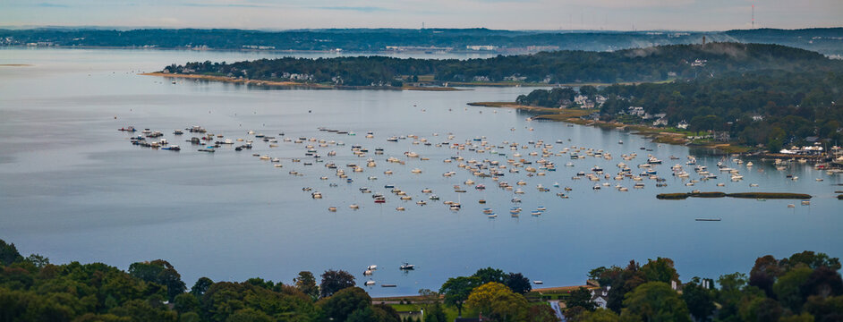 Aerial view of boats dotting the tranquil waters, framed by lush greenery under a hazy sky, creating a serene maritime panorama, Duxbury, Massachusetts, United States.