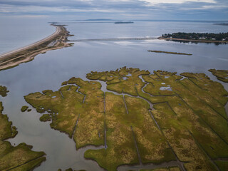 Aerial view of the vast marshland's green and gold hues meeting the tranquil, reflective waters, a long, sandy causeway slicing through the bay, Duxbury, Massachusetts, United States.