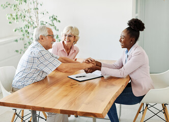 Portrait of a businesswoman or real estate agent shaking hands with senior couple in her office or at their home