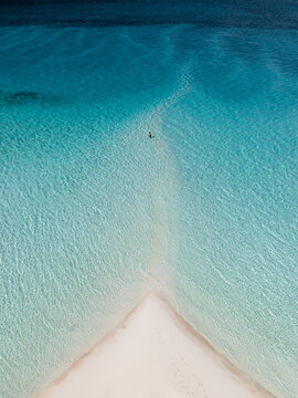 Aerial view of turquoise waters gently meeting the pristine white sand, creating a serene coastal scene, Great Harbour Cay, Berry Islands, The Bahamas.