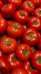 Bright red tomatoes stacked together, showing smooth glossy skin and fresh green stems.
