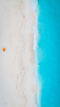 Aerial view of turquoise waves gently kissing the pristine white sand where a solitary orange umbrella stands out, Zakynthos, Greece.