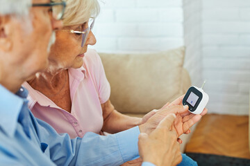 Portrait of senior couple using lancet on finger for checking blood sugar level with glucose meter. Healthcare and medical, diabetes, glycemia concept