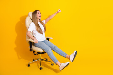 Happy young woman in a white t shirt and jeans sits in an office chair on a bright yellow...